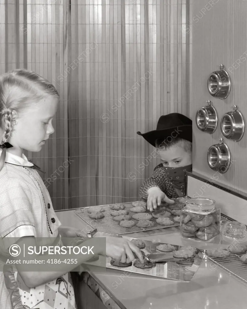 1960S Blond Girl Taking Cookies Off Tray At Kitchen Counter Younger Boy With Cowboy Hat And Bandana Mask Reaches To Steal Them