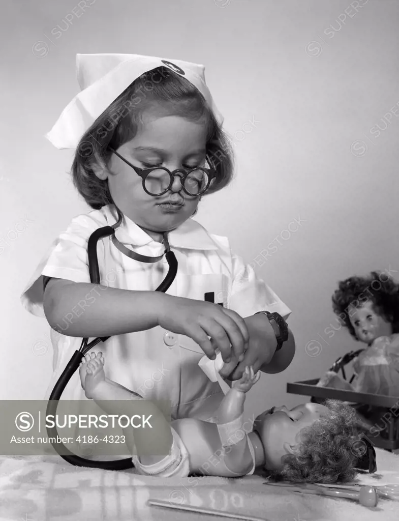 1950S 1960S Girl Wearing Nurse Uniform Eyeglasses Putting Bandage On Doll'S Arm  