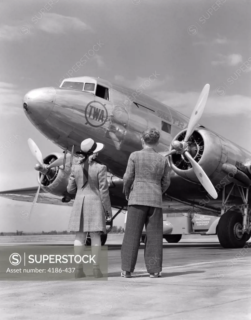 1940S Rear View Of Boy & Girl Standing Together Looking At Propeller Airplane Outdoor