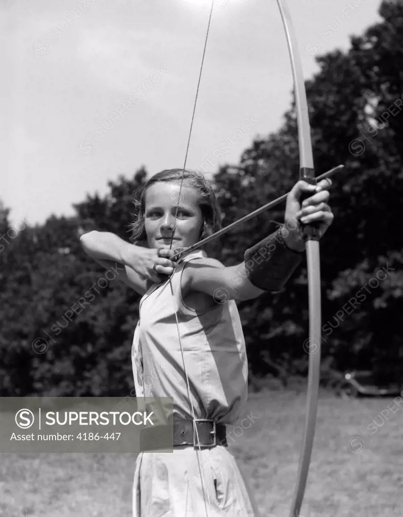 1930S Girl Wearing A Camp Jumper With Wide Leather Belt About To Release An Arrow From Bow