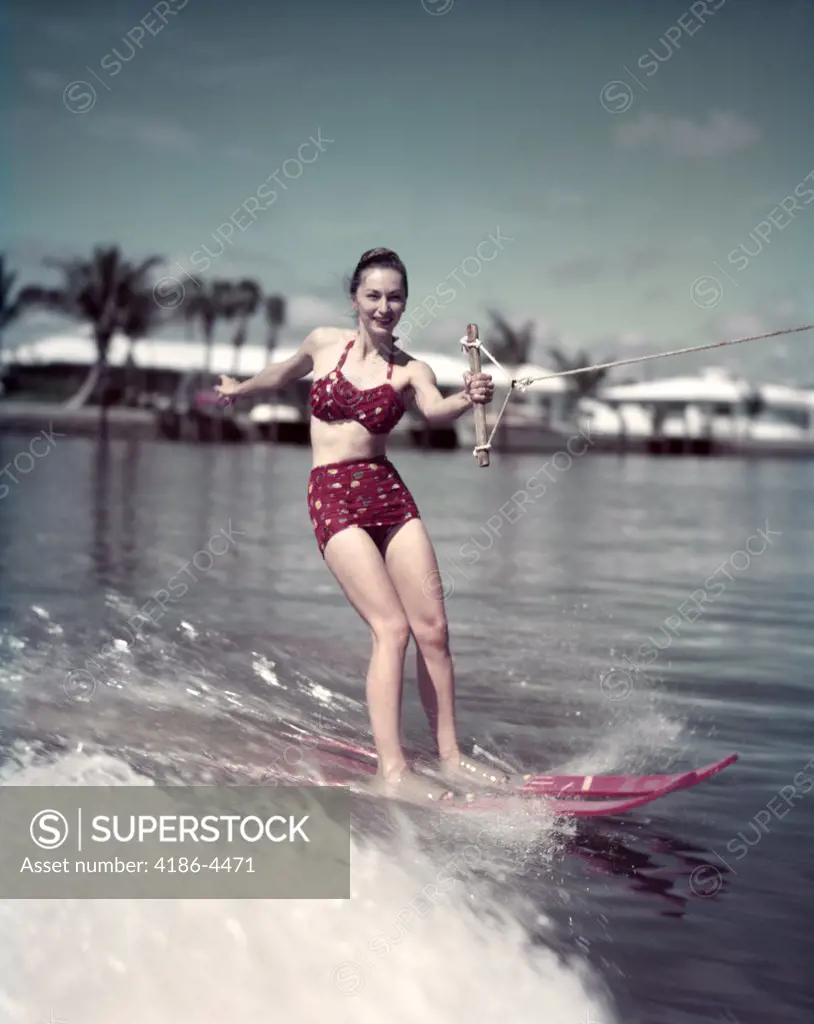 1950S Smiling Woman Wearing Red Two Piece Bathing Suit Holding Tow Rope Water Skiing Past Tropical Water Front Homes And Palms Florida Usa