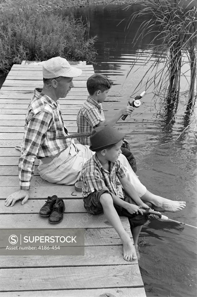 1950S 1960S Father With Two Sons Sitting On Dock Fishing Together Outdoor By Pond