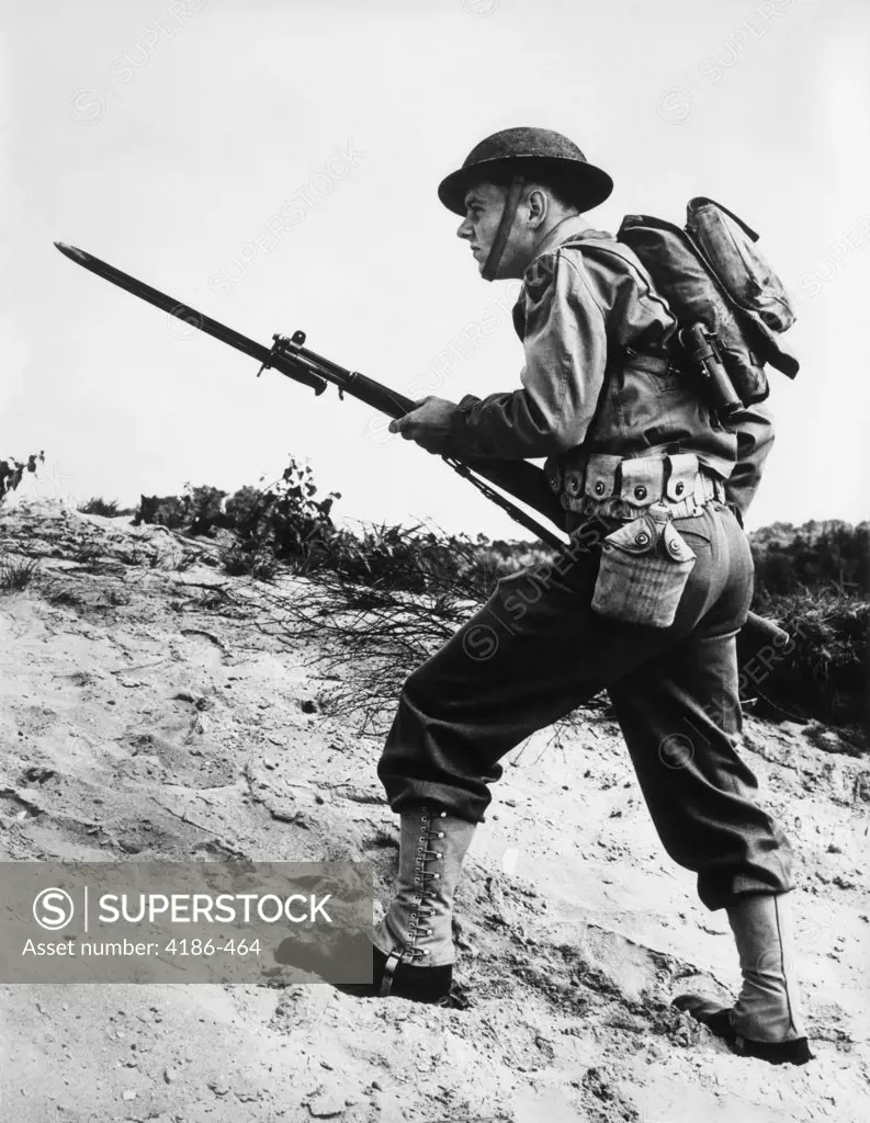 1940S 1942 World War Ii Soldier Walking Across Rough Terrain With Rifle And Bayonet In Hand