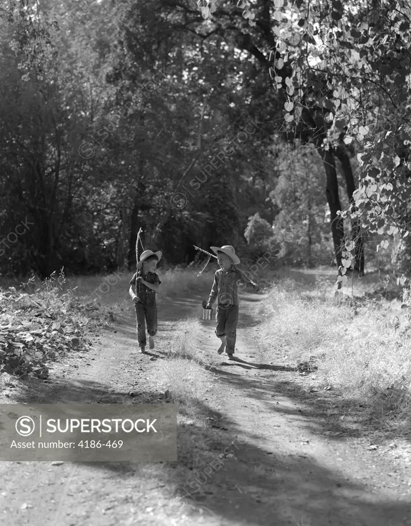 1940S 1950S Two Boys In Dungarees Plaid Shirts Straw Hats Walking Down Dirt Road Carrying Fishing Poles & Can Of Bait