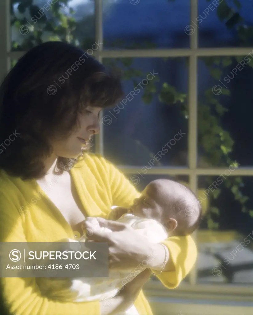 1970S Mother Holding Newborn Baby By Window