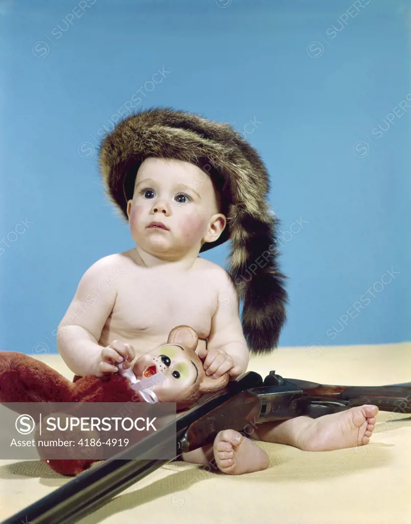 1960S Baby Boy Wearing Coonskin Cap With Stuffed Animal And Shotgun Gun