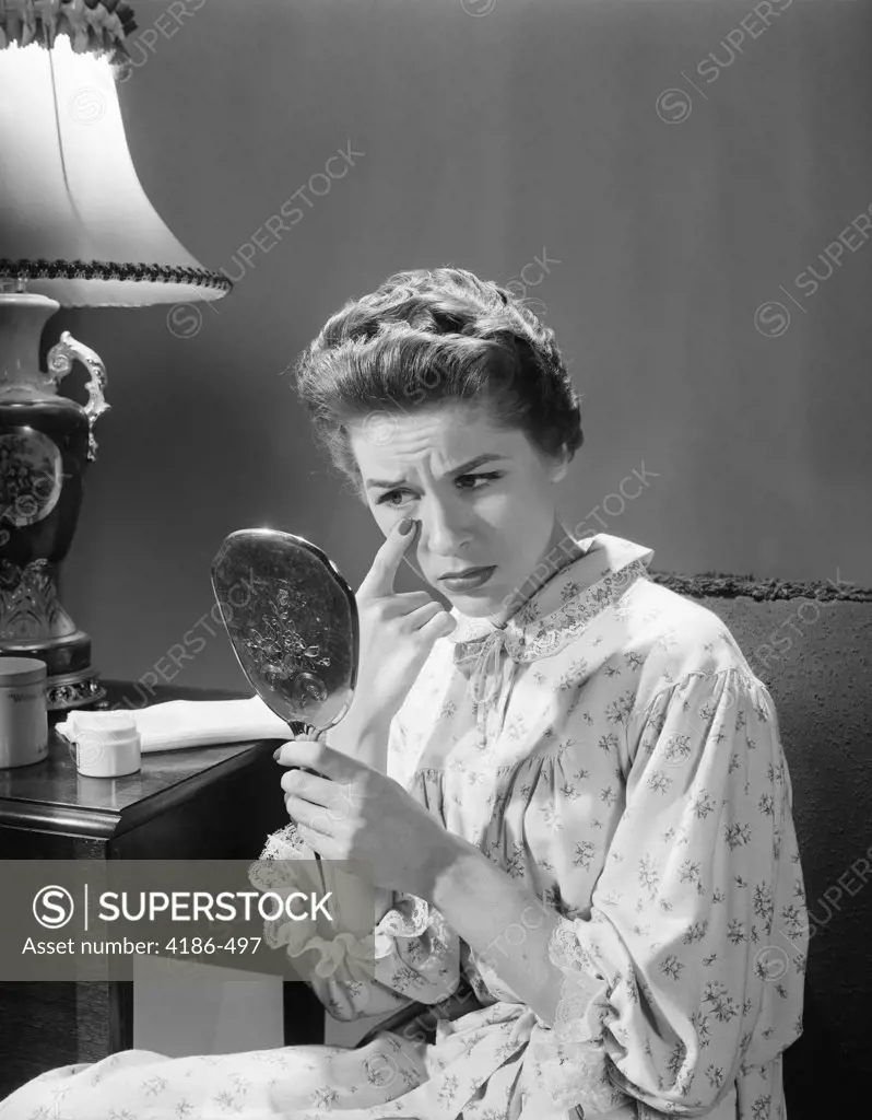 1950S 1960S Woman In Nightgown Holding Mirror Look At Eye Wrinkles Aging Beauty Cosmetic Serious Concerned Expression