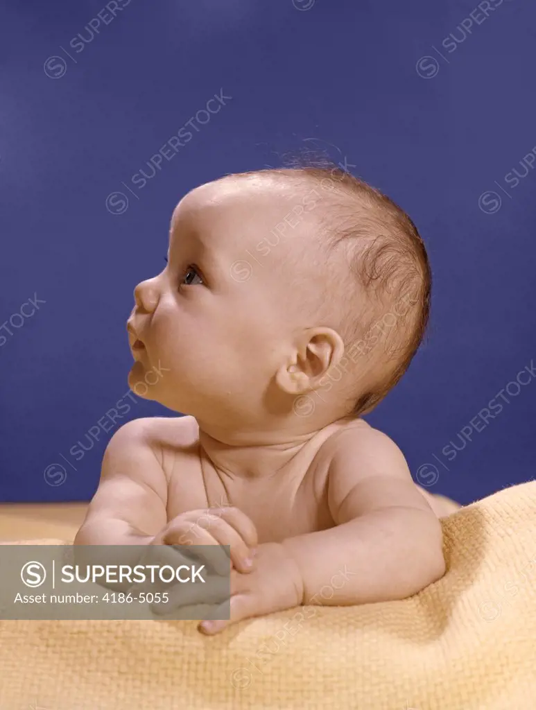 1960S Portrait Of Baby On Yellow Blanket Resting On Folded Arms Head Turned To Right Looking Up
