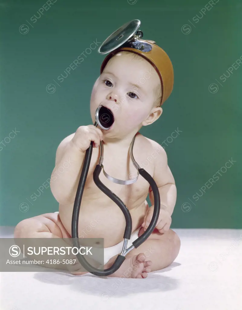 1960S Baby Dressed As Medical Doctor Wearing Opthalmoscope And Putting Stethoscope In Mouth