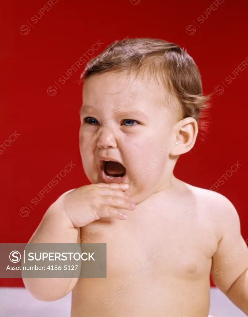 1960S Portrait Of Crying Baby Holding Hand Up To Mouth Red Background