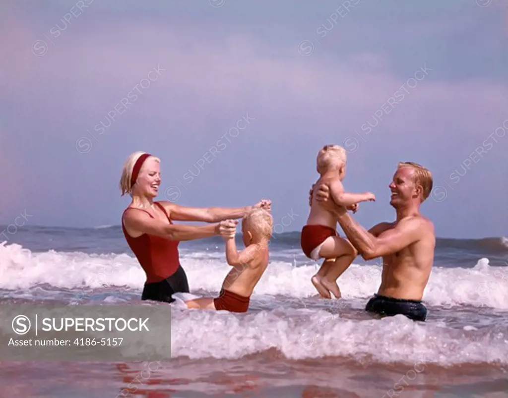 1970S Family Father Mother Two Sons Laughing Hand Holding Jumping In Ocean Surf At Beach Having Fun Together