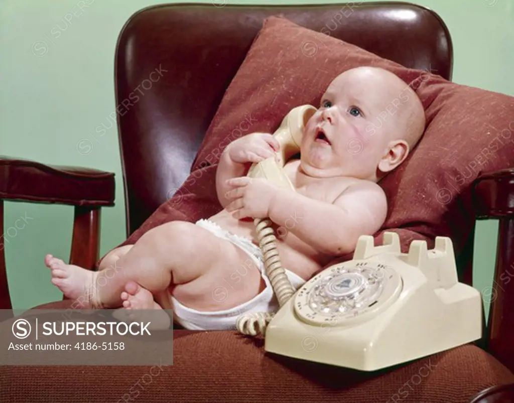 1960S Baby In Office Chair Propped On Pillow Talking On Telephone
