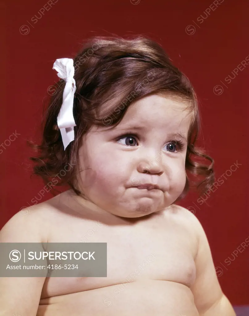 1960S Portrait Of Chubby Unhappy Baby Girl With White Ribbon Bow In Messy Hair