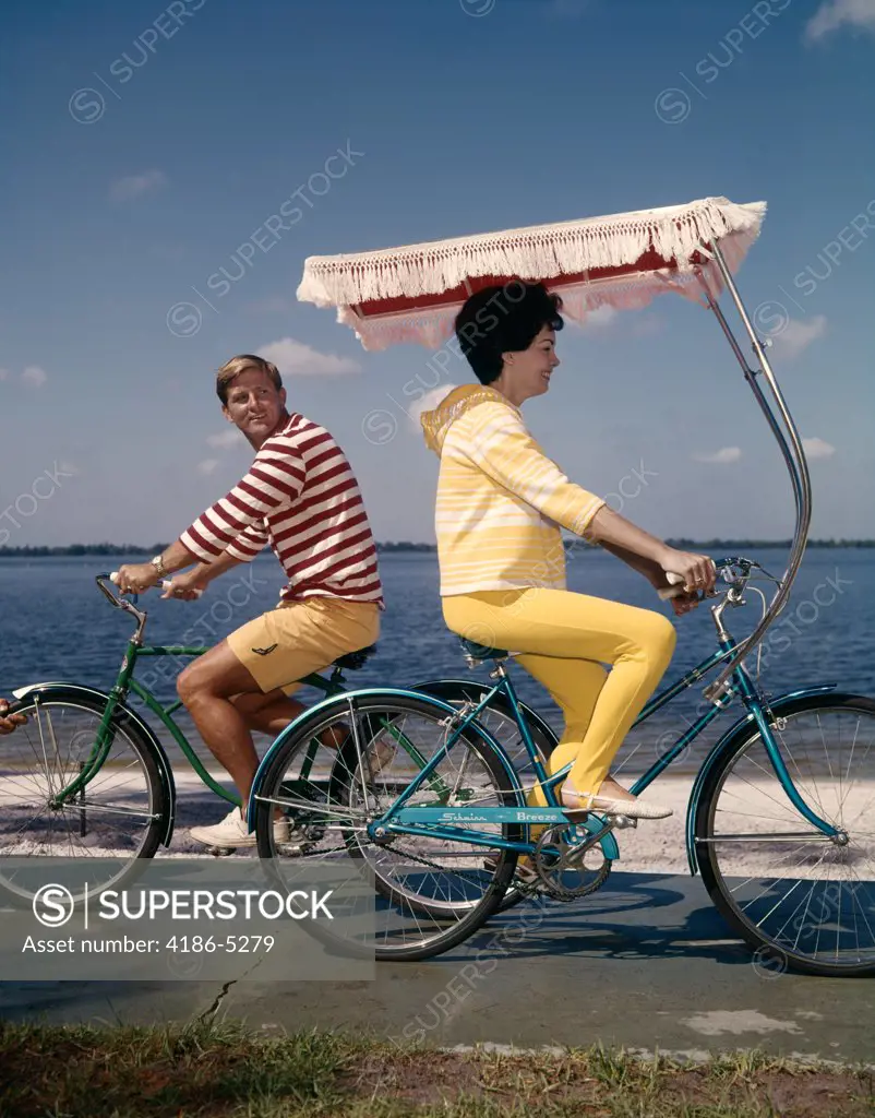 1960S Woman And Man Riding Bicycles Going In Opposite Direction Near Water  
