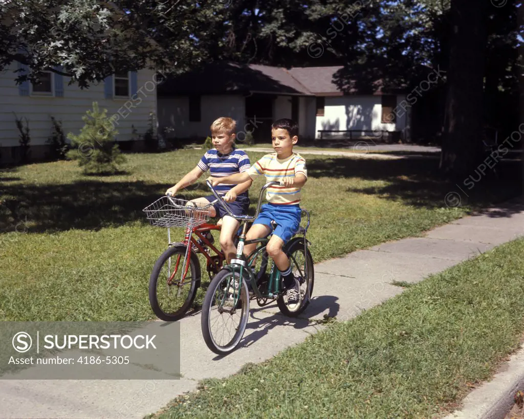 1970S Two Boys Riding Bikes Down Suburban Neighborhood Sidewalk