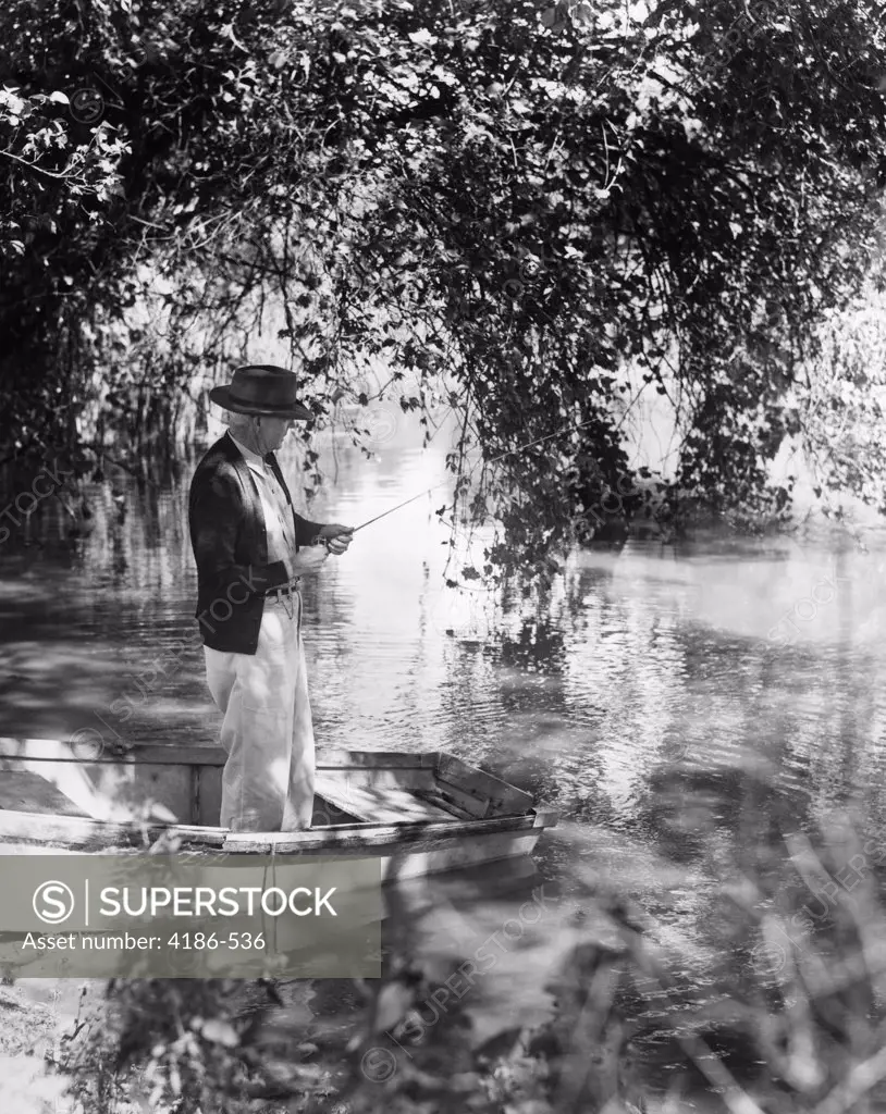 1940S Elderly Man In Hat Standing In Rowboat Fishing Under Trees