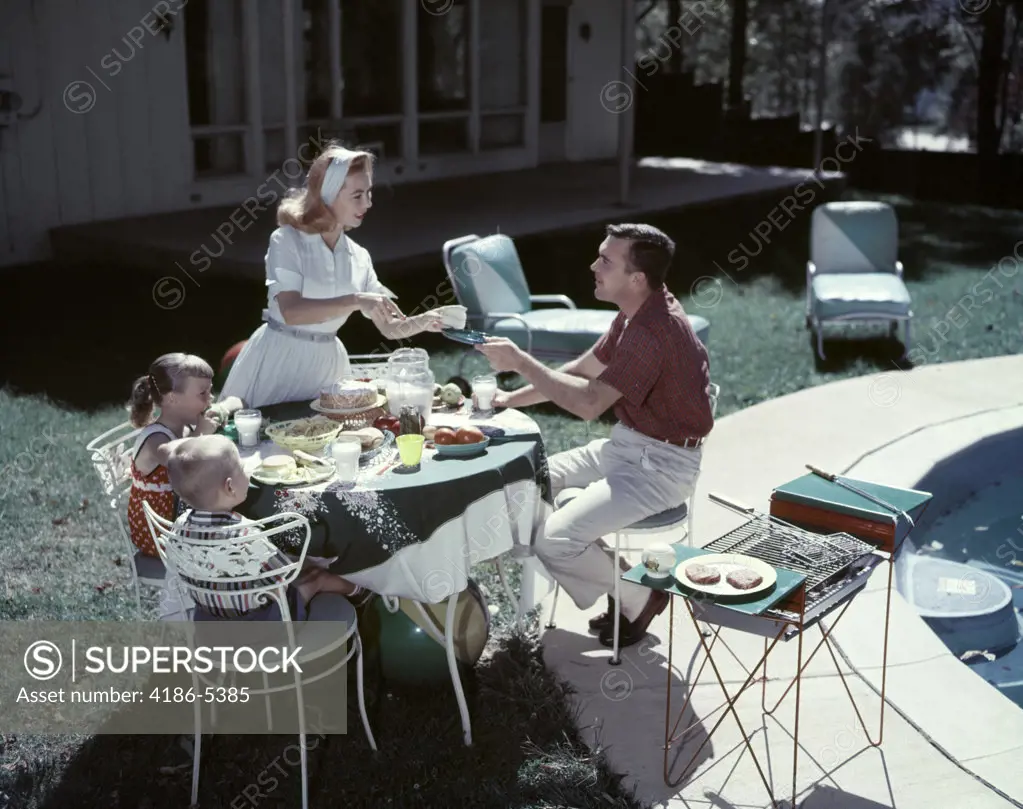 1950S Family In Backyard Having Picnic From Grill Near Swimming Pool