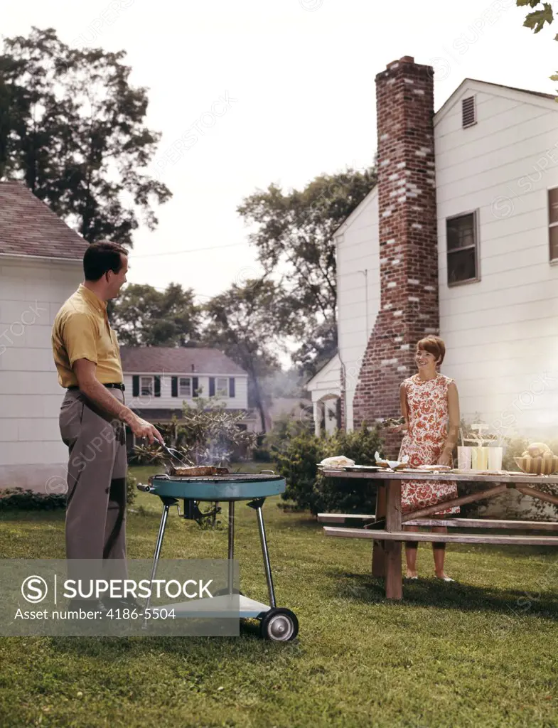 1960S Couple Suburban Backyard Man Grilling Woman Setting Picnic Table