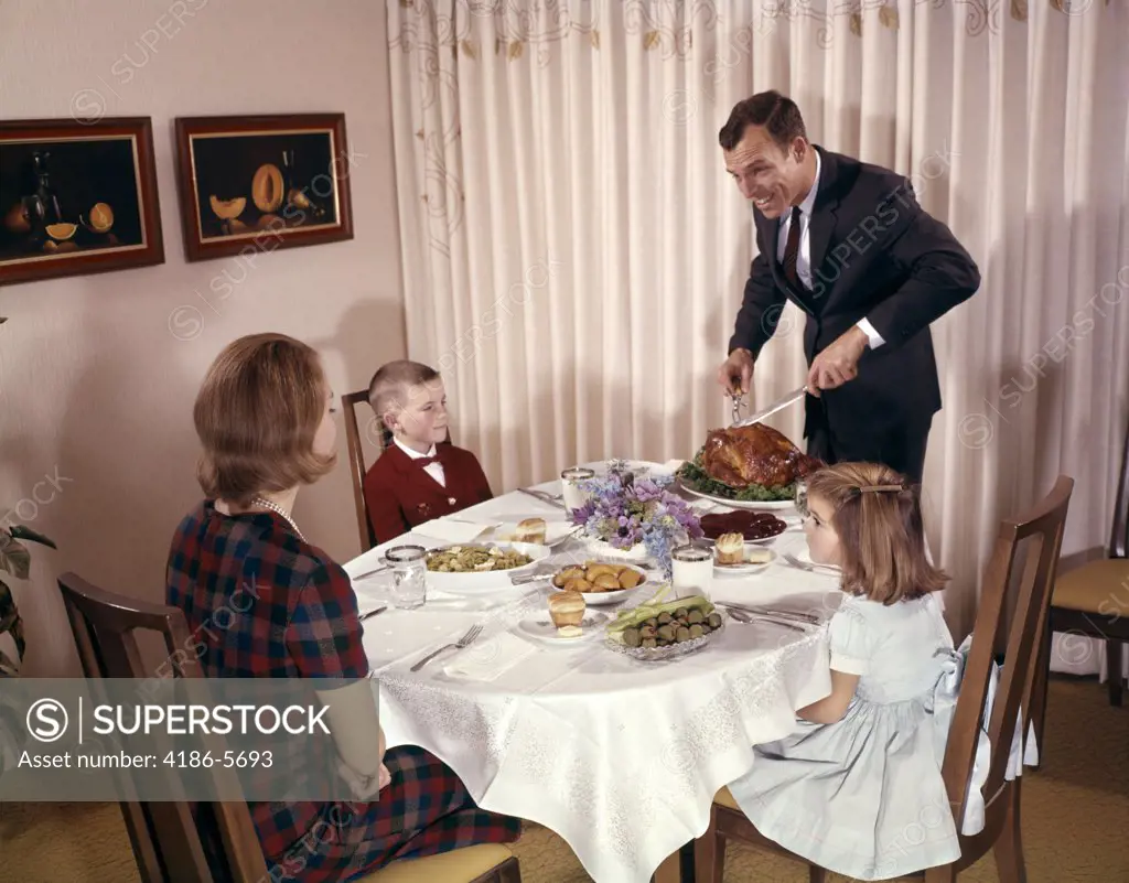 1960S 1970S Woman Mother Boy Son And Girl Daughter Sitting At Dining Room Table Watching Man Father Carve Turkey For Thanksgiving Dinner