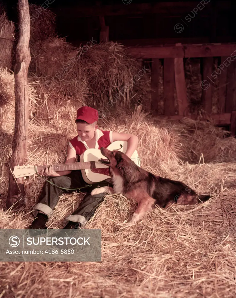 1950S Boy Playing Guitar Collie Dog Sitting Hay Bales Inside Barn  