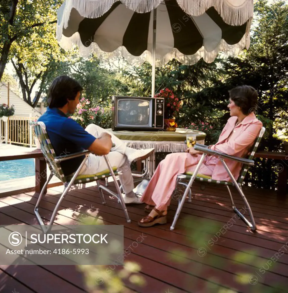 1970S Pool Lifestyle Couple Man Woman Sitting Patio Table Umbrella Shade Watching Portable Tv Television