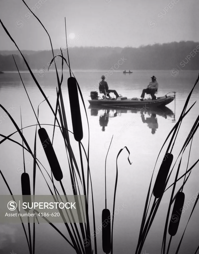 1980S Two Men In Bass Fishing Boat On Calm Water Lake Cattails In Foreground