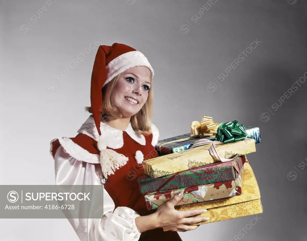 1960S Young Woman In Red And White Santa Helper Costume And Hat Holding Pile Of Wrapped Christmas Presents Studio