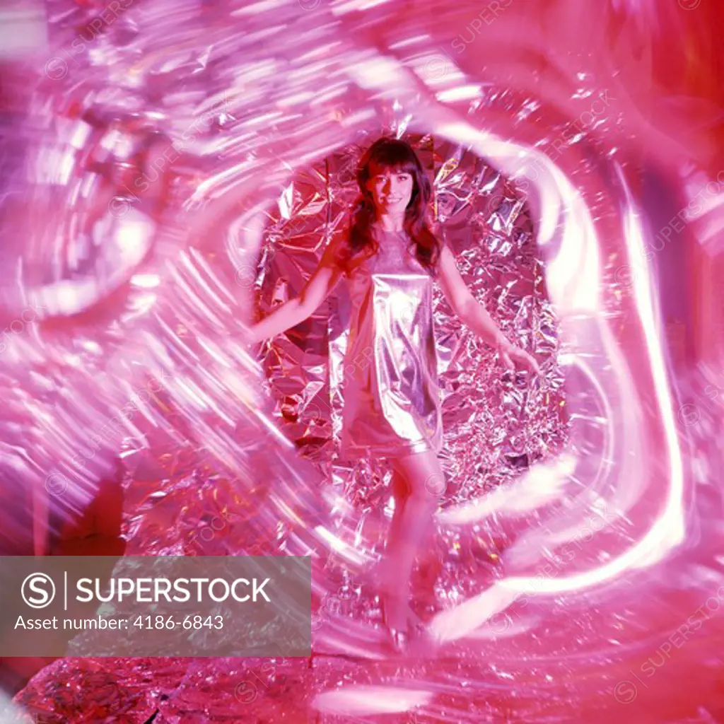 1960S 1970S Smiling Woman With Long Brunette Hair In Short Silver Lame Miniskirt Dress Dancing Amid Swirling Red Light And Foil Backdrop