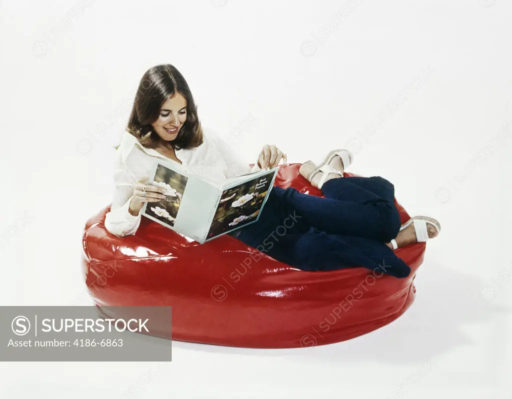 1960S 1970S Woman Smiling Reading Book Reclining In A Red Beanbag Chair 