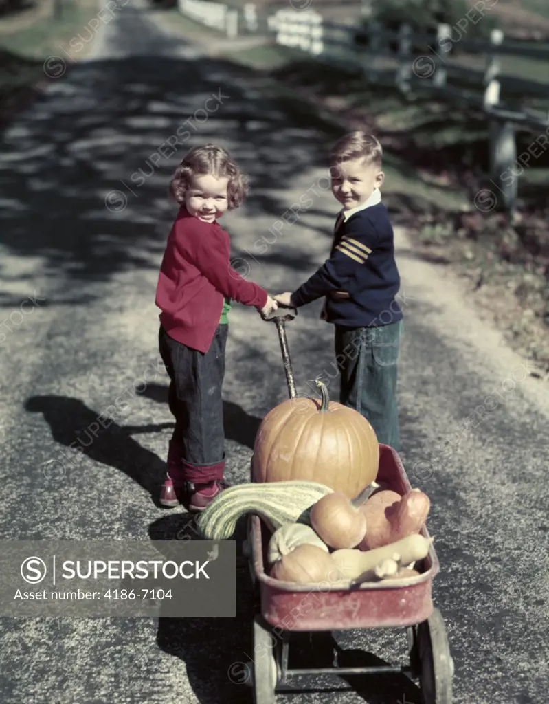 1950S Two Smiling Young Kids Boy Girl In Blue Jeans Pulling Red Wagon Full Of Harvest Pumpkins And Gourds