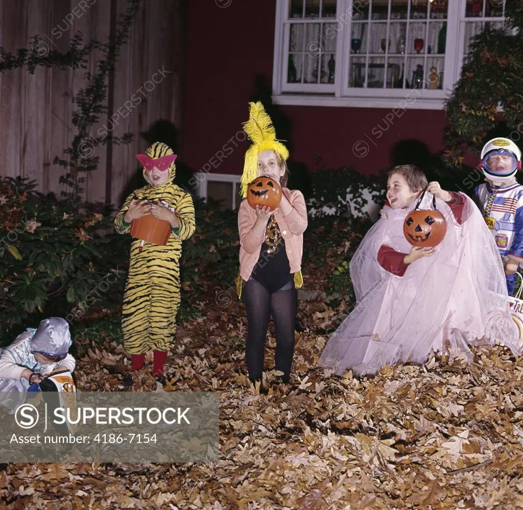 1970S Group Of Five Boys And Girls In Halloween Costumes Holding Trick Or Treat Pumpkins And Bags In Front Yard Of House