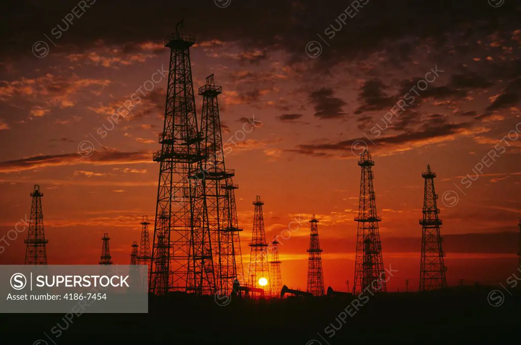 Derricks And Pumps In Oil Field At Sunset