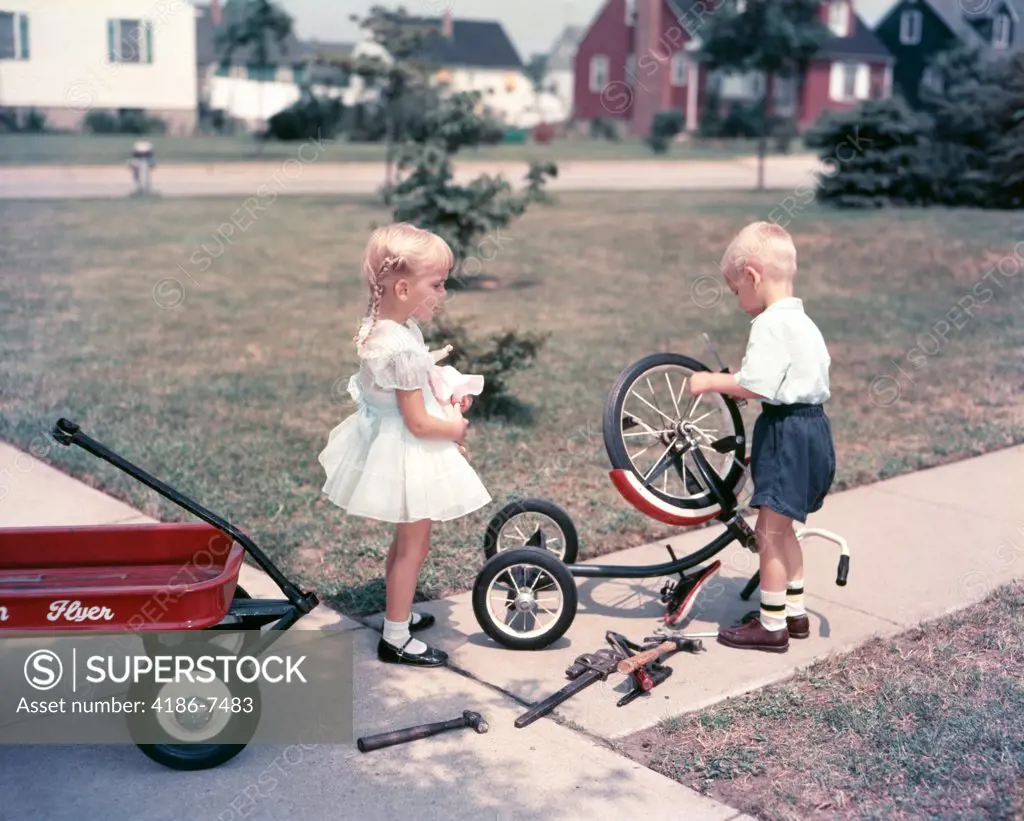 1950S Little Blonde Girl Sister Holding Doll Watching Little Boy Brother Repair Tricycle 