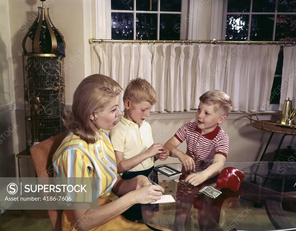 1960S Mother And Two Sons Counting Money From Piggy Bank On Glass Table