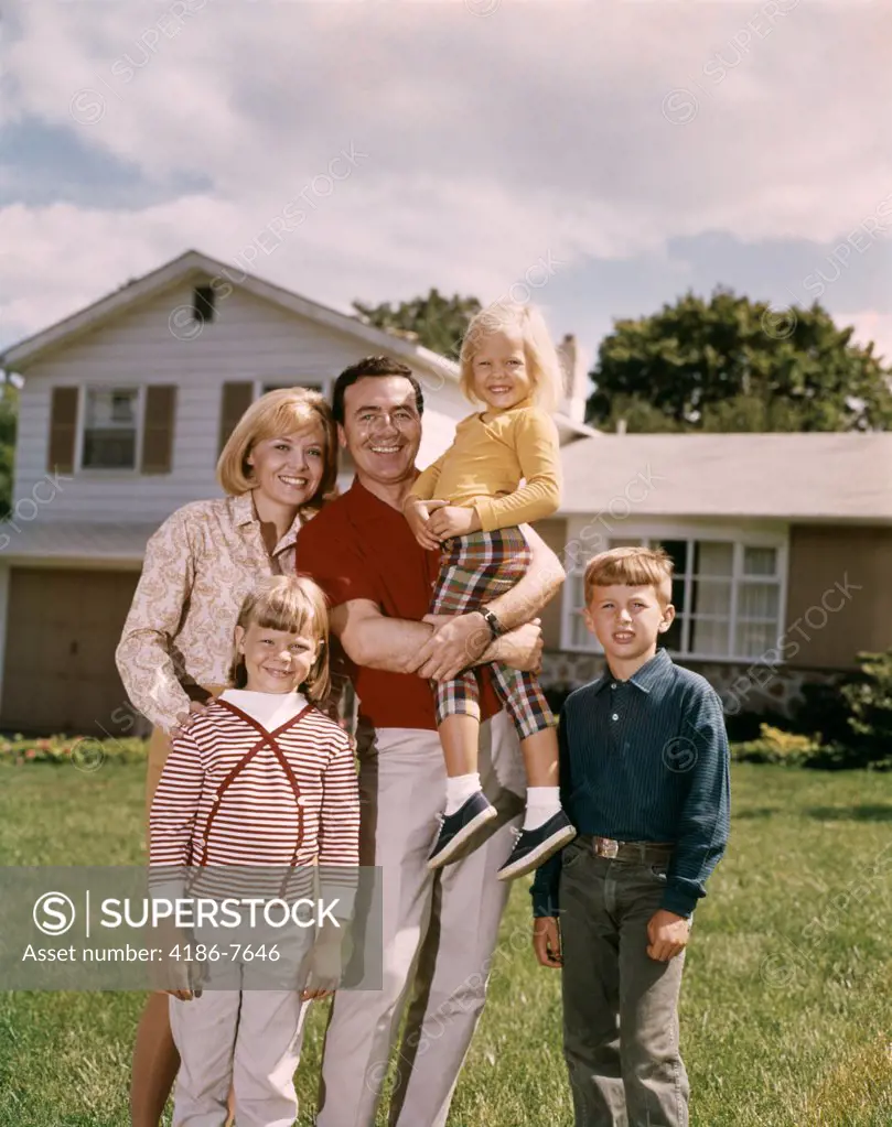 1960S Smiling Family Portrait Standing In Front Of A Suburban Split Level House Father Mother Two Daughters And Son 