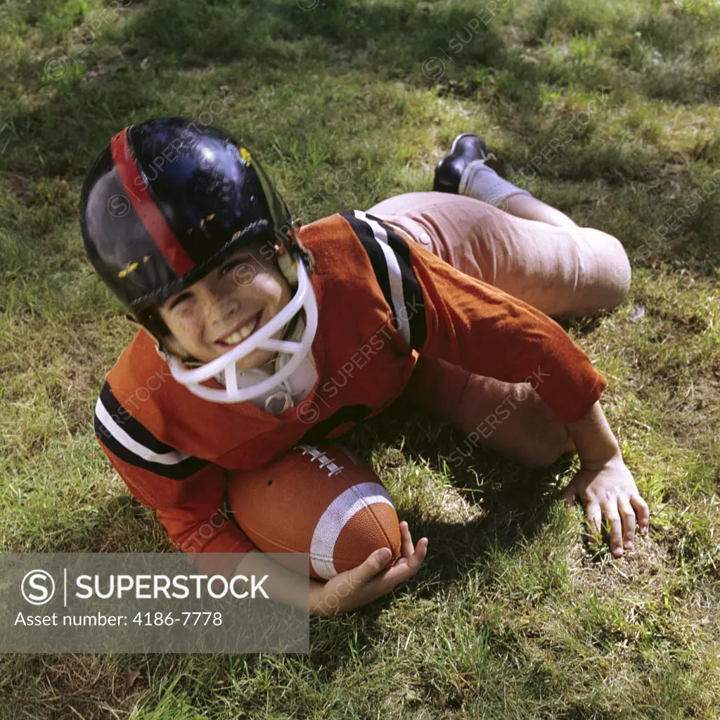 1970S Freckle Faced Boy Football Uniform Helmet Orange Top Lying In Grass Holding Football Looking Up