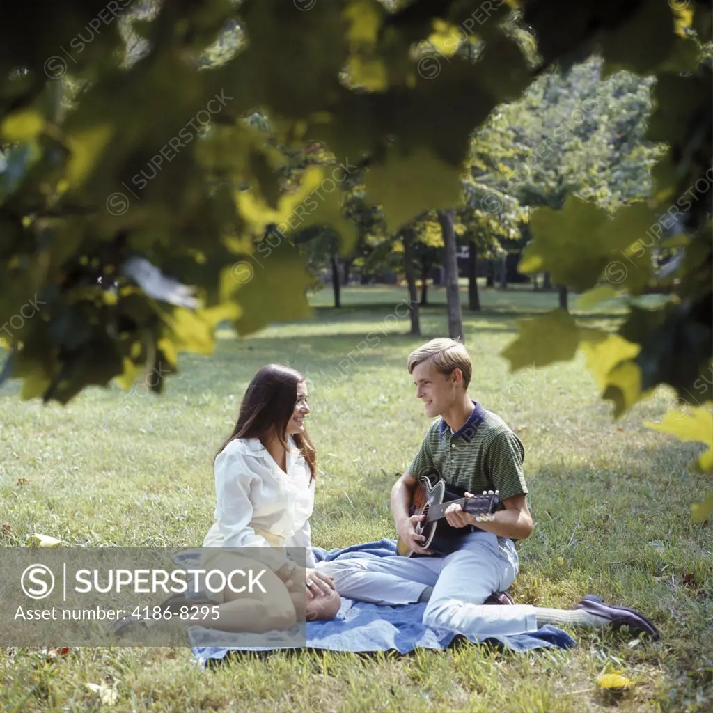1960S 1970S Smiling Couple Sitting On Blanket On Grass Man Playing Acoustic Guitar
