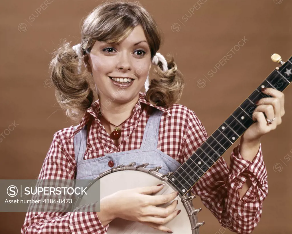 1970S Young Woman In Checked Shirt And Overalls With Hair In Ponytails Playing Banjo Strum Rube Bumpkin Country