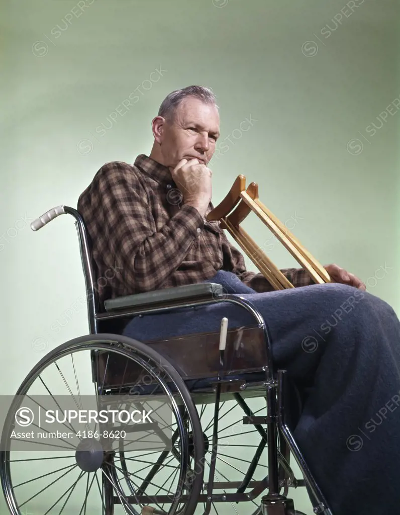 1960S Sad Senior Man Sitting In Wheelchair With Crutches Blanket Wrapped Around Legs