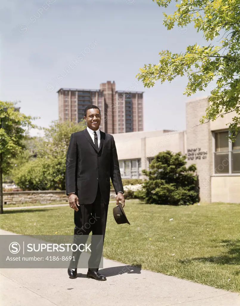 1960S African American Business Man Holding Briefcase And Hat Walking On Urban Sidewalk