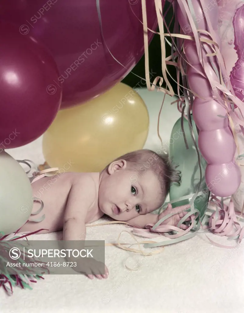 1950S Baby Lying On White Blanket Amid Pink Yellow Red New Year Balloons And Streamers Party Celebration