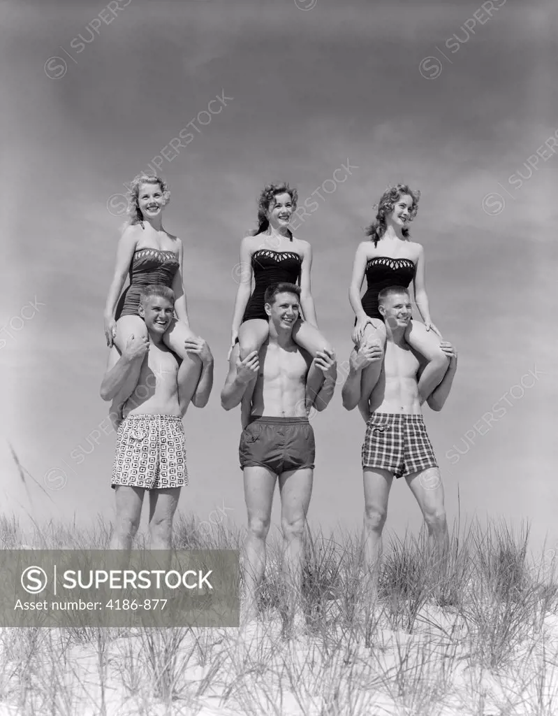 1950S 1960S Three Couples At Beach On Dunes With Women In Identical Bathing Suits Sitting On Men'S Shoulders