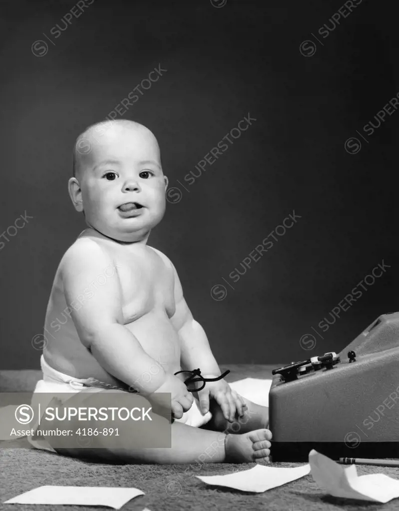 1950S 1960S Baby In Diaper Sticking Out Tongue Holding Glasses Sitting Before Adding Machine
