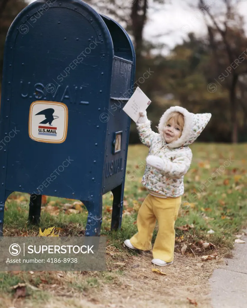 1970S Smiling Toddler Girl Wearing Hooded Jacket Reaching Up To Mail Letter In Mail Drop Box