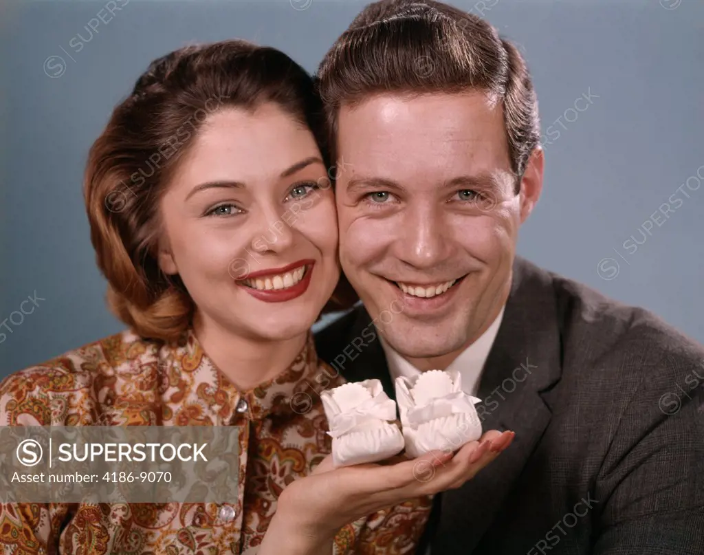 1960S Smiling Couple Holding Baby Shoes 