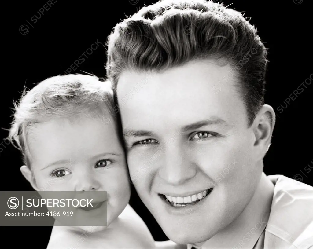 1940S Portrait Of Smiling Father Holding Baby Daughter To Cheek