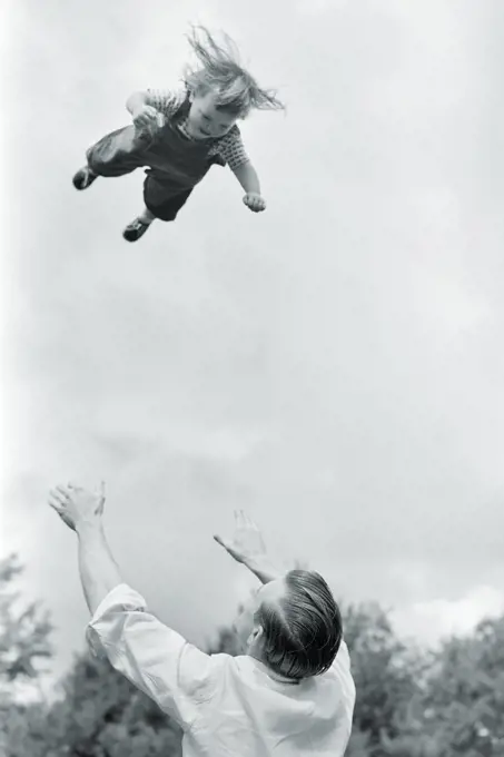 1950s 1960s FUN OR DANGEROUSLY FOOLISH FATHER THROWING TODDLER DAUGHTER HIGH INTO THE AIR AND WAITING TO CATCH HER COMING DOWN