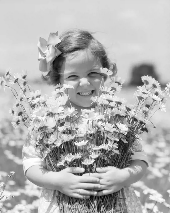 1930s SMILING HAPPY LITTLE GIRL LOOKING AT CAMERA HOLDING A BIG BUNCH OF FRESHLY PICKED DAISIES FLOWERS
