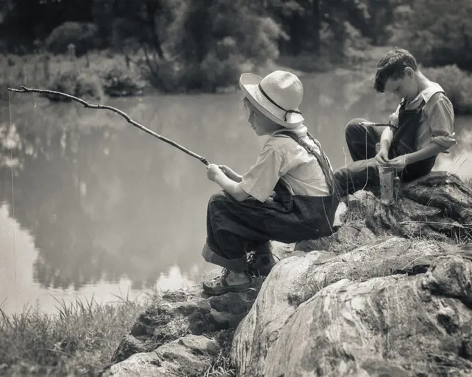 1930s  TWO BOYS  SITTING ON ROCKS FISHING IN POND WITH POLES MADE FROM TWIGS AND STRING