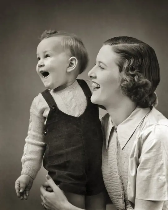 1940s LAUGHING BABY BOY TODDLER STANDING SUPPORTED BY SMILING MOTHER